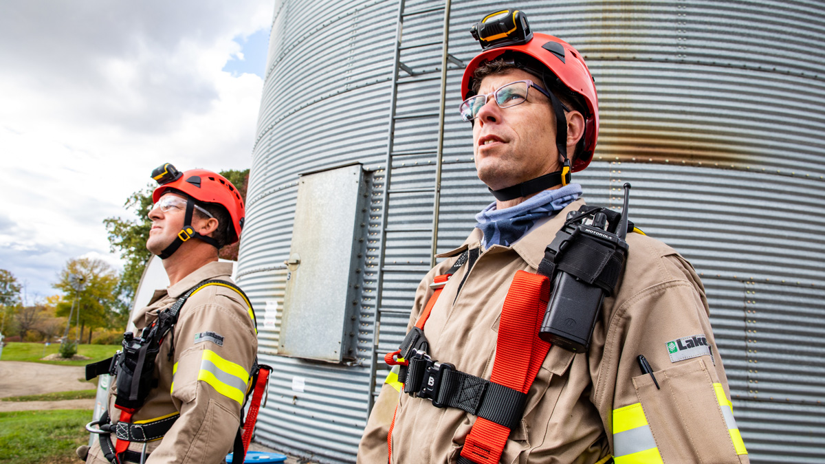 Two firefighters standing in PPE beside grain silos